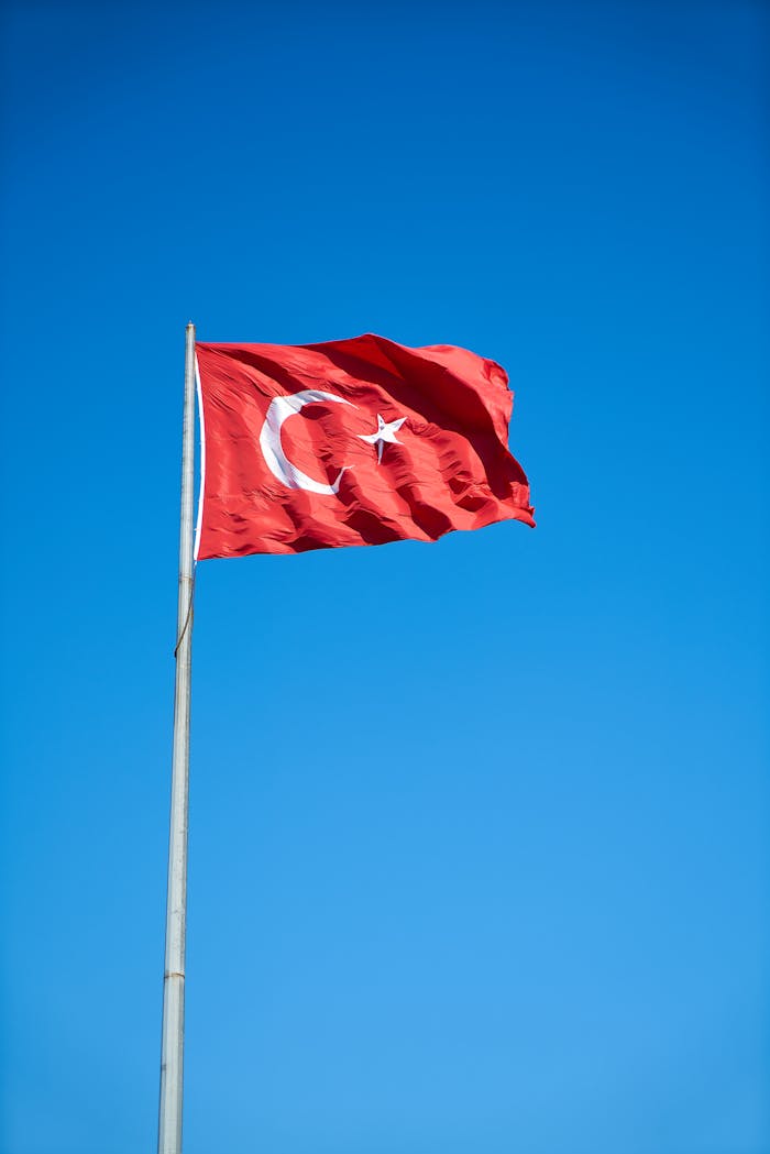 Vibrant Turkish flag waving on a flagpole against a cloudless blue sky symbolizing freedom and patriotism.